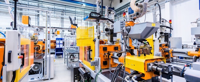 Horizontal color image of large group of automated injection moulding machines for plastic parts production. Powerful molding machinery in factory arranged in a row.